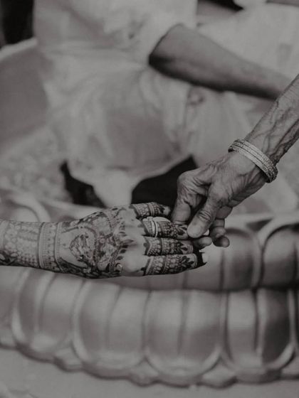 A powerful black and white photo of a young hand with intricate henna being held by an older, wrinkled hand, symbolizing the passing of blessings through generations.