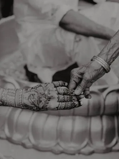 A powerful black and white photo of a young hand with intricate henna being held by an older, wrinkled hand, symbolizing the passing of blessings through generations.