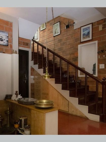 The area under a staircase is utilized for displaying traditional brass vessels, blending utility and decor.