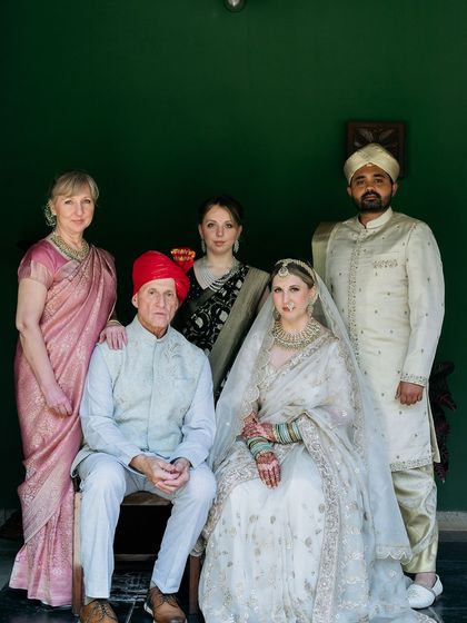 A formal family portrait from a cross-cultural wedding, with the bride's family from the West and the groom's family in traditional Indian wear.