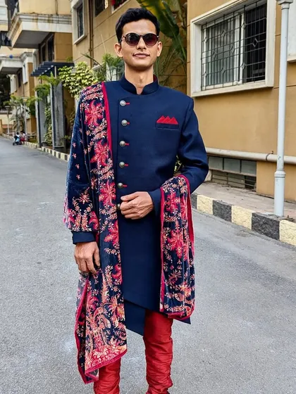 My men's collection includes modern ethnic wear like this navy blue Indo-Western sherwani. The look is elevated with a beautifully printed velvet stole, perfect for groomsmen or wedding guests.