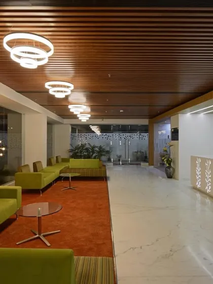 A large reception space featuring a custom-designed desk with botanical motifs. The area combines a formal waiting lounge with an orange carpet and a more casual seating area with green sofas.