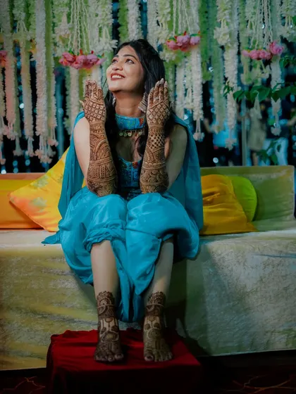 A full length portrait of the bride, happily showing off her beautiful mehndi on her hands and feet.
