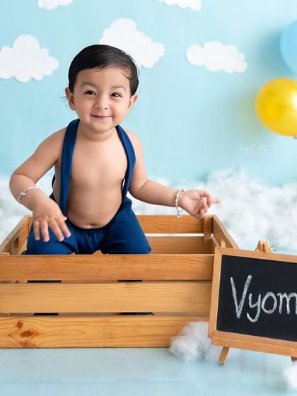 A smiling baby poses next to his nameplate during his sky-themed sitter session.