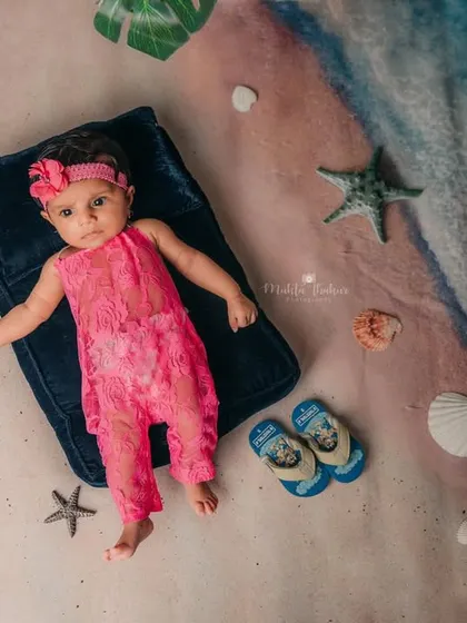 This four-month-old is enjoying her 'beach day' in the studio, surrounded by shells and starfish on a sandy backdrop.