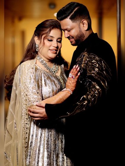 A happy couple sharing a moment. The groom looks dashing in a black velvet jacket with bold, abstract gold embroidery, a design that is both modern and luxurious.