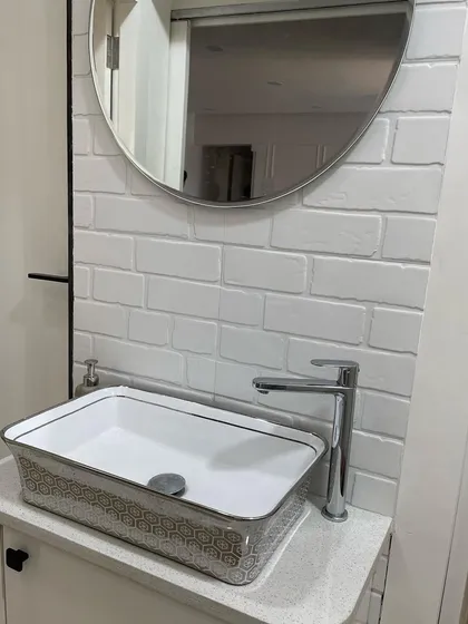 This stylish washbasin area is located in a common passage, proving you can add function anywhere. The design features a modern patterned vessel sink, a simple round mirror, and a white brick tile backsplash for a touch of texture.