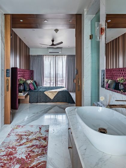 The master bedroom of the Filigree House, viewed from the bathroom. The rich burgundy headboard and layered textiles create a sense of depth and luxury, perfectly framed by the open doorway.