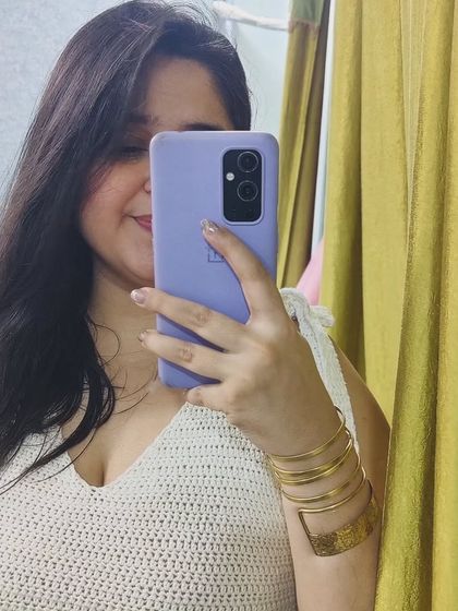 A mirror selfie showing off a white crochet top I made. It features a V-neck and shoulder ties, making it a trendy and comfortable piece for summer.