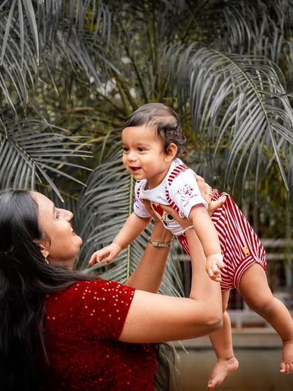 A joyful mother lifts her baby up in the air during an outdoor shoot. The selective color effect highlights their connection against the monochrome background.