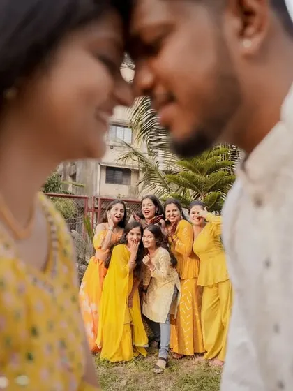 A creative and romantic shot, with the couple in the foreground and their cheering friends blurred in the back, telling a story of love and friendship.
