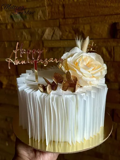 This anniversary cake features delicate wafer paper ruffles and is topped with a single cream rose and gold accents.