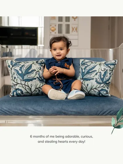 Six months of being adorable and curious. A simple, candid shot at home showing the baby's personality as she sits on a miniature sofa.
