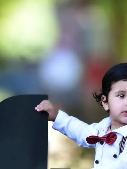 A close up portrait of a little boy dressed smartly in a bow tie and suspenders for his first birthday photoshoot with the mini piano prop.