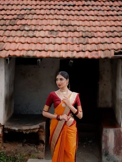 A wide shot of a model in a traditional saree standing before a rustic village house. This composition tells a story of heritage and timeless elegance.