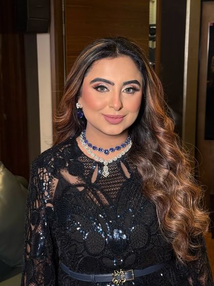 A close-up of a glamorous evening look. The makeup features a soft smokey eye and a nude lip, paired with voluminous curls and a statement sapphire necklace.