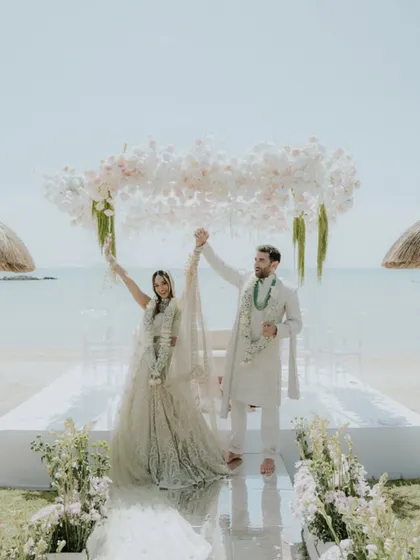 The couple celebrating under their floral mandap after the ceremony in Mauritius. This wide shot, featured in Vogue India, showcases the beautiful beachside setting and the happiness of the newlyweds.