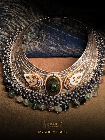 A bold, oxidized silver collar necklace, or hasli, featuring intricate carvings, a central gemstone, and cascading beadwork. A true statement of power and style.