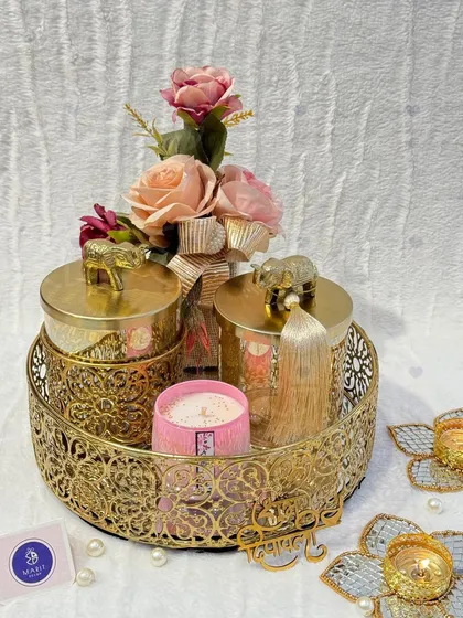 A luxurious golden Diwali hamper. This set features two ornate jars with elephant-topped lids, a scented candle, and flower-shaped 'diya' holders on a carved metal tray.