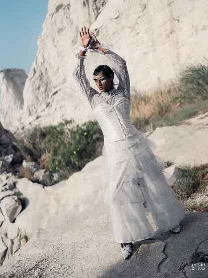 This wide shot places the avant-garde feather look within a natural, rocky landscape, creating a beautiful contrast between the delicate styling and the rugged environment.