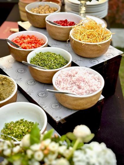 A vibrant array of fresh chaat toppings. Bowls are filled with finely chopped onions, tomatoes, herbs, and crispy sev, allowing guests to customize their snacks at our interactive station.