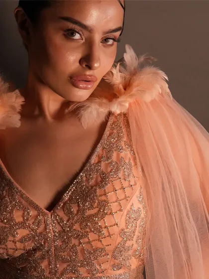 It's all in the details. A close-up of the peach gown, showing the delicate beadwork and the soft feather and tulle cape. This straight-fit outfit is available to rent or buy.