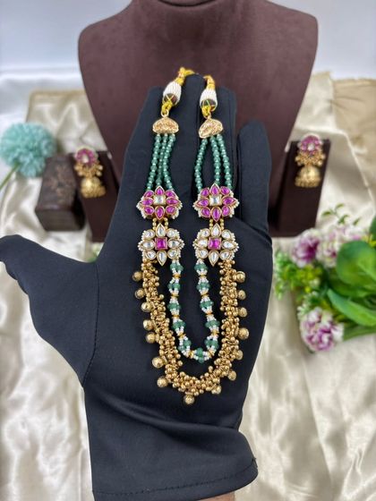 The Rishika premium antique gold set. It features a unique double-layer design with one layer of golden beads and another of green beads, adorned with floral motifs in pink stones.
