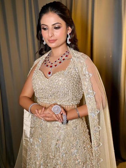 The full look, featuring a stunning ivory and gold lehenga with dramatic ruby jewellery. The makeup is glamorous and sophisticated.