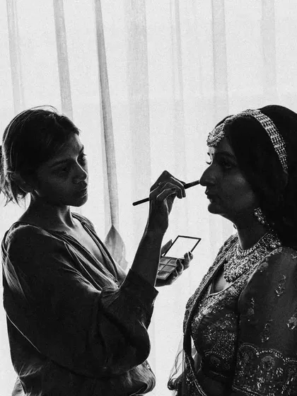 A black and white shot of the bride, Maitri, getting her makeup done. The silhouette effect against the window creates a timeless and artistic feel.