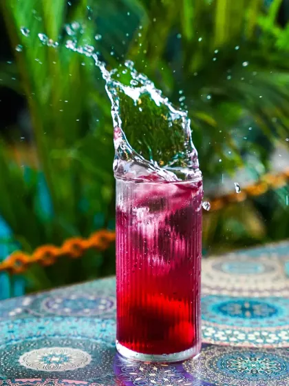A dynamic action shot capturing the perfect splash in a vibrant red cocktail against a lush green background. This kind of high-speed beverage photography is ideal for creating exciting visuals for bar menus and social media campaigns.