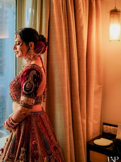 A candid shot of the bride looking out the window, her deep red floral bun adding to the romantic mood.