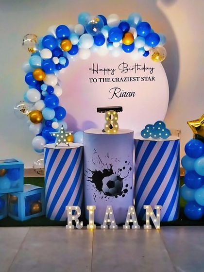 A sporty football-themed birthday party in blue, white, and gold. The decor features a circular backdrop, striped plinths with a football graphic, and star-shaped balloon accents.