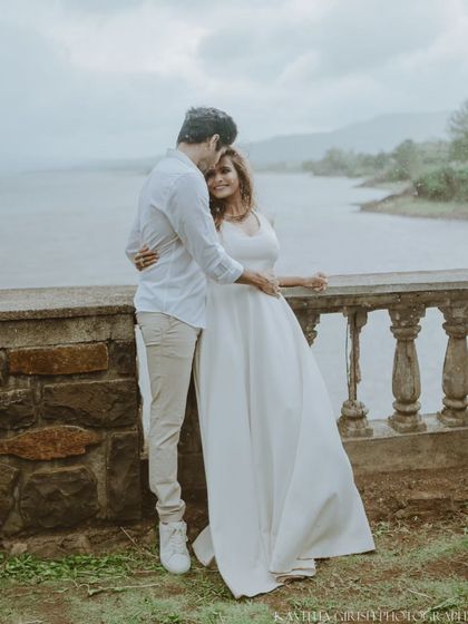 A full-length portrait of a couple in coordinated white outfits, sharing a quiet moment by the water. This showcases a classic, timeless pre-wedding photography style.