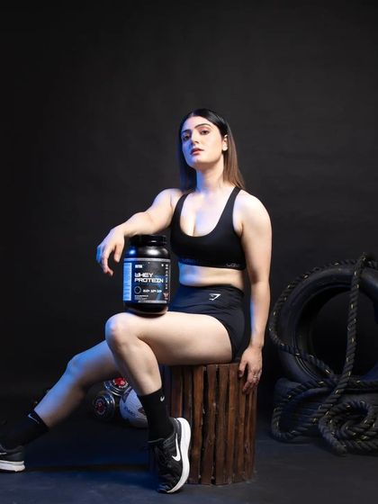 A portrait of a female fitness model with the whey protein product. The pose is confident and aspirational, and the lighting highlights both the model's physique and the product's branding. This type of shot works well for social media content and brand storytelling.