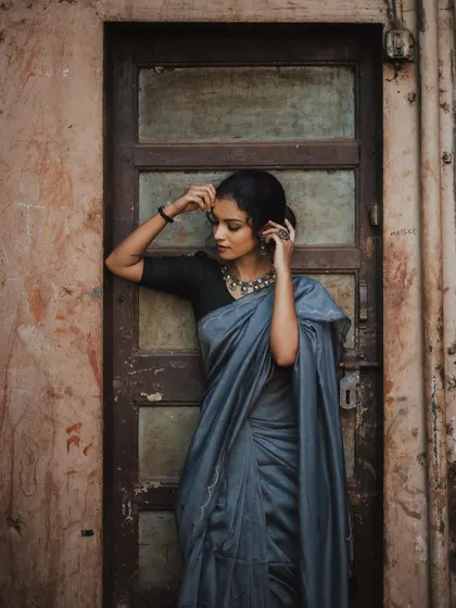 A vertical full-length shot that emphasizes the model's graceful posture against a rustic wooden door. The soft lighting and her contemplative pose make for a timeless and elegant portrait.