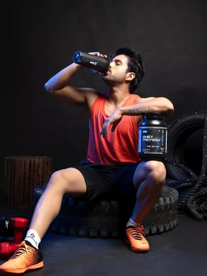 This shot shows the product in use, with the model drinking from a shaker bottle while resting on a tire. The main product container is clearly visible, creating a narrative of use and recovery that is highly relatable for the target audience.