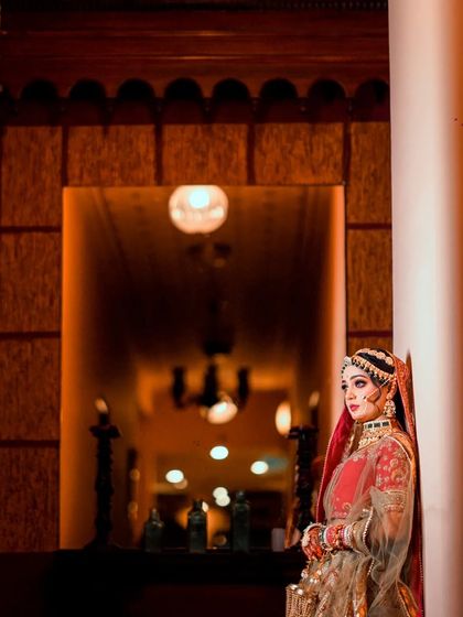 A wide shot of the bride in a grand hallway. The warm, ambient lighting and architectural details create a royal and majestic feel.