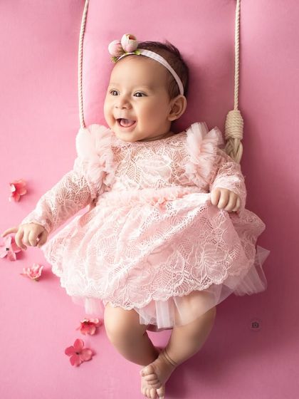 A moment of pure joy. This baby girl breaks into a wide, happy laugh during her photoshoot on the pink floral swing.