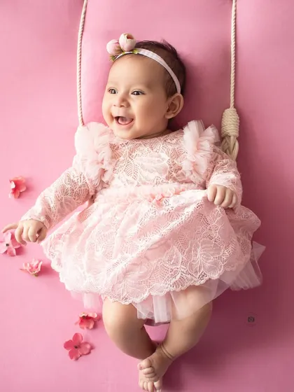 A moment of pure joy. This baby girl breaks into a wide, happy laugh during her photoshoot on the pink floral swing.