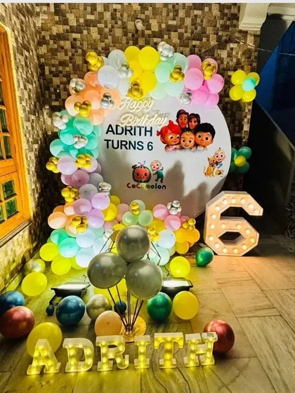 A colorful Cocomelon theme for Adrith's 6th birthday. This outdoor setup includes a themed backdrop, a pastel balloon garland, a light-up number '6', and light-up letters spelling the name.