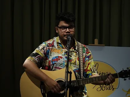 A musician in a cool comic-themed shirt plays his guitar and sings.