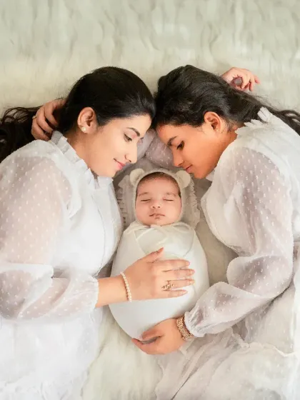 An angelic overhead shot of a mother and older sister watching over their new baby. Coordinated outfits and serene expressions make this a truly special family heirloom.