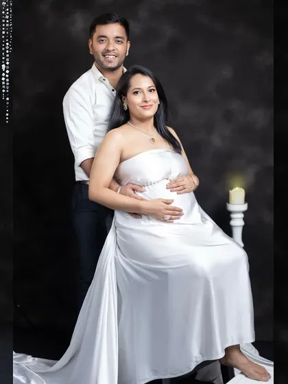 A formal seated portrait of the couple. The mom-to-be is radiant in a white satin gown, creating a look of pure elegance and serenity.