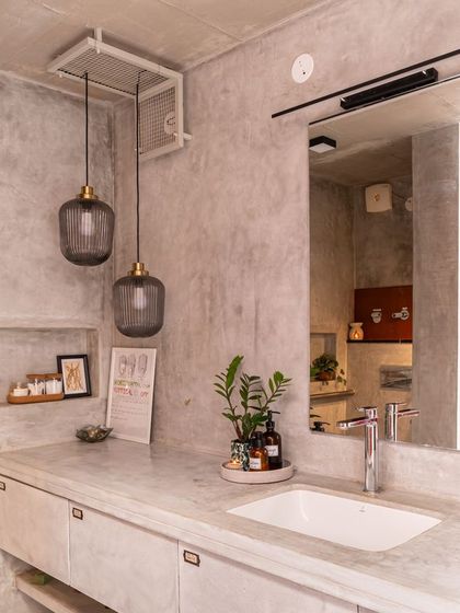 The main bathroom vanity is crafted from polished cement, creating a seamless, monolithic look. Smoked glass pendant lights and simple accessories complete this minimalist and functional space.