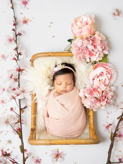 Pretty in pink. This newborn girl is swaddled and sleeping in a bamboo basket, framed by beautiful cherry blossoms for a delicate and artistic portrait.