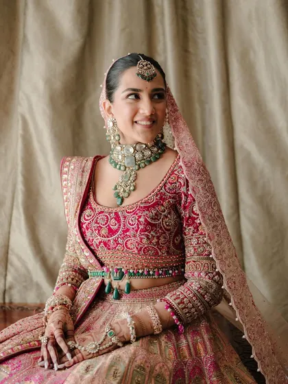 A bride's happy smile. This portrait captures the joy of the moment, with her radiant expression complemented by the soft pink and jewel tones of her Tarun Tahiliani lehenga and emerald jewelry.