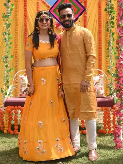 A classic couple portrait from their Haldi ceremony, dressed in coordinated yellow outfits against a festive backdrop.