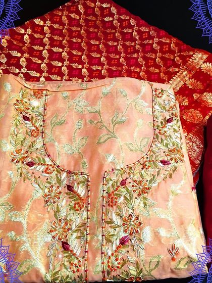A beautiful peach-colored unstitched suit with intricate embroidery. It is paired with a rich red Banarasi dupatta, making it a perfect choice for weddings and festivals.