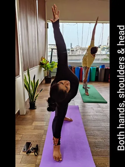 A perfect Trikonasana (Triangle Pose) requires alignment. Notice how the student's hands, shoulders, and head are in one straight line. This precision is what makes the pose effective for stretching the entire side of the body.