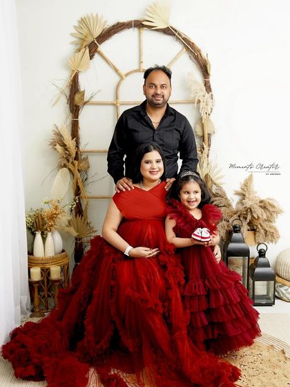 A stunning family maternity portrait in coordinated red gowns. The older sister holds a pair of tiny shoes, a sweet symbol of the new life they are all excited to welcome.